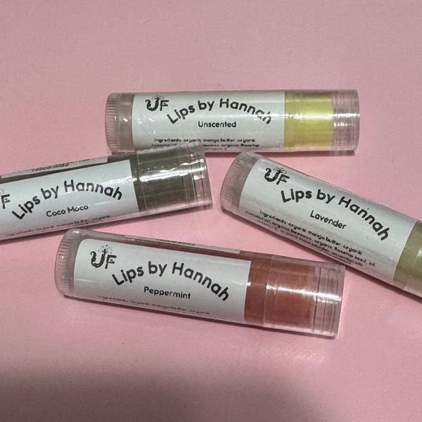 Four lip balm tubes labeled "Lips by Hannah" in various flavors on a pink background.
