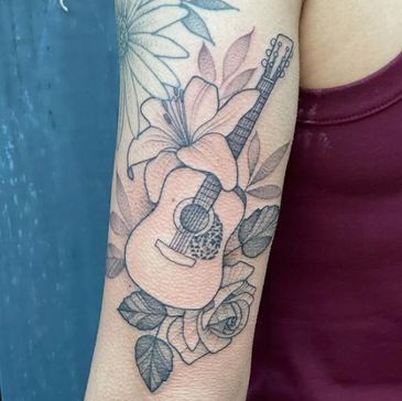 Black and gray tattoo of a guitar surrounded by flowers on an arm.