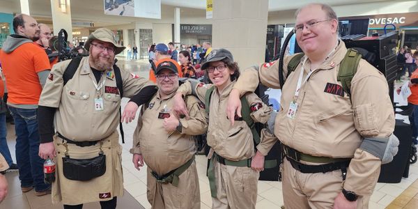 Four men dressed as Ghostbusters in a busy shopping mall.