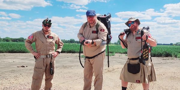 Three men dressed as Ghostbusters outdoors on a sunny day.