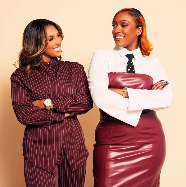 Two confident women smiling at each other, dressed stylishly in maroon and white.