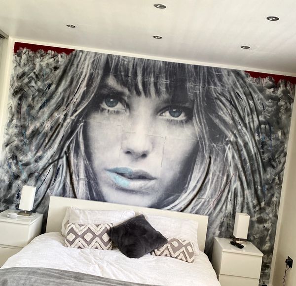 A modern bedroom with a large black-and-white mural of a woman's face behind the bed.