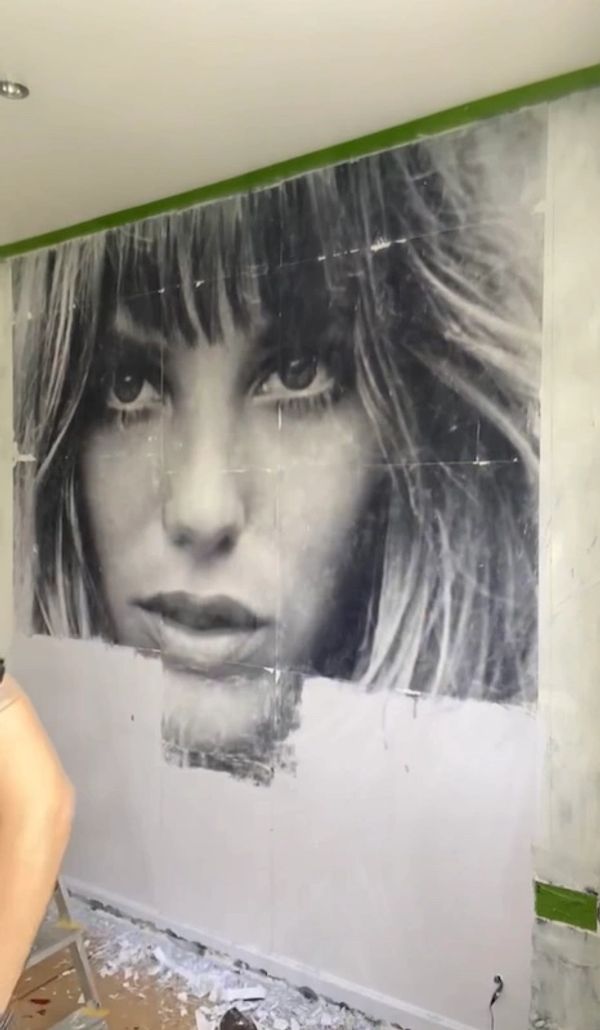 Black and white mural of a woman's face being painted on a wall.