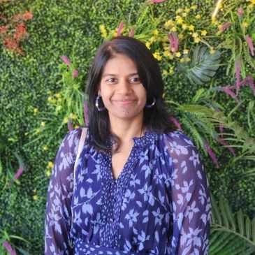 Woman smiling in front of a vibrant green and floral backdrop.