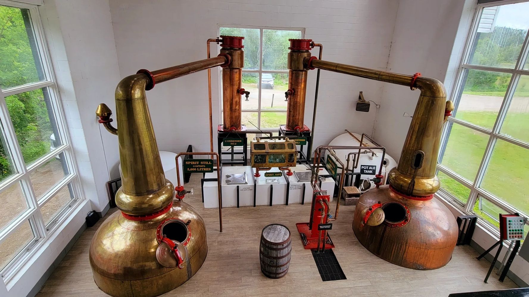 Copper pot stills inside a distillery with labeled tanks and barrels.