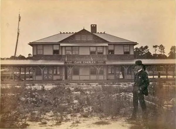 Historical photo of a train station with a man standing in front.