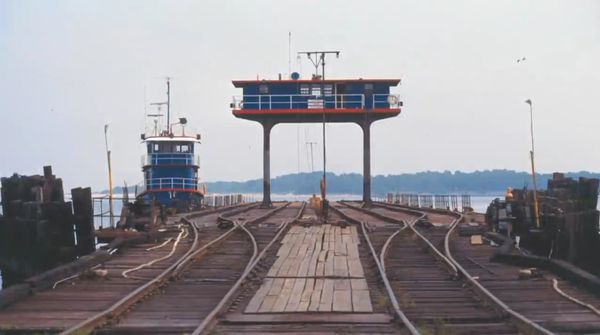Old railway tracks leading to a blue and red structure by the water.