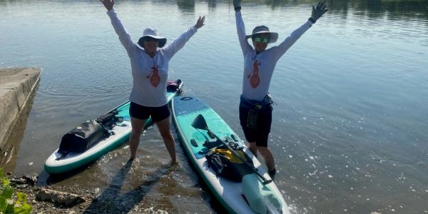 Two people celebrating by the water with paddleboards.