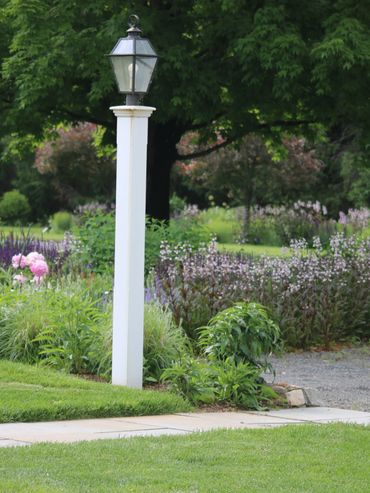 White garden lamp post surrounded by greenery and flowers.