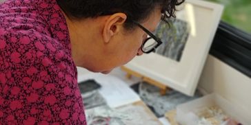 Person wearing glasses and a pink patterned shirt, working on an art project.