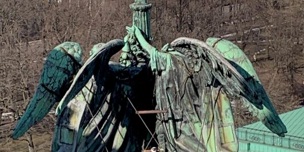 Close-up of a weathered bronze eagle statue with spread wings.