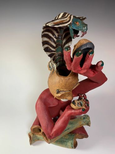Colorful sculpture of a red-armed humanoid with a cobra head and mask.