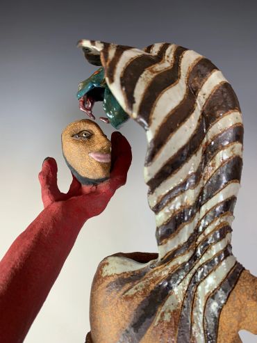 Abstract sculpture with a striped figure and red arm holding a small face.