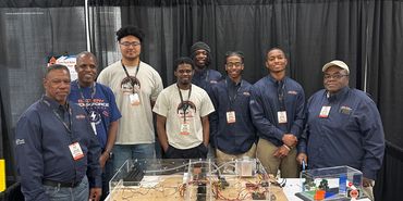 A group of men posing behind a robotics project at a science fair.