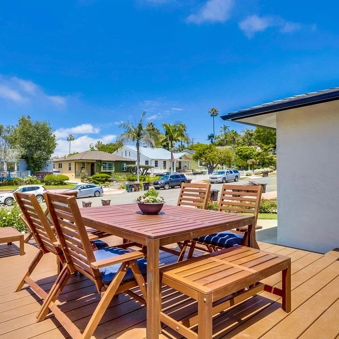Wooden outdoor dining set on a sunny deck with a neighborhood view.