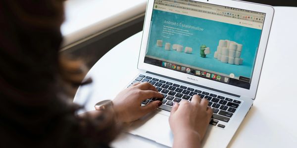 Person typing on a laptop showing Android 6.0 Marshmallow webpage.