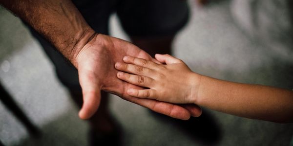 An adult and child touch hands in a gesture of connection.