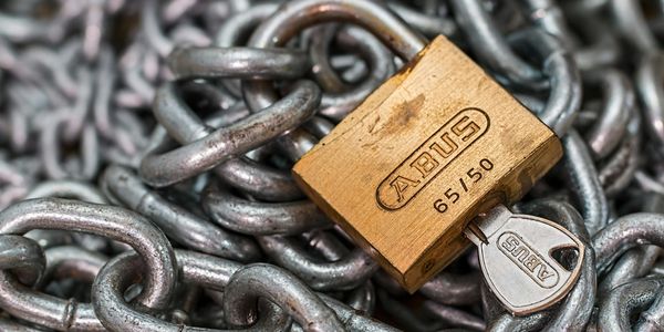 A brass ABUS padlock secured with a key among metal chains.