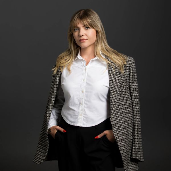 Confident woman in white shirt and plaid blazer against dark background.