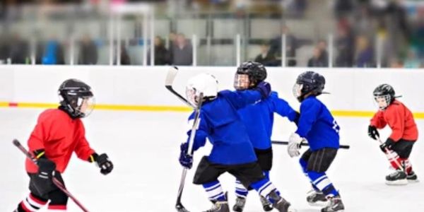 Kids playing ice hockey in red and blue uniforms on an indoor rink.