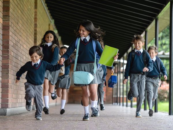 Happy schoolchildren in uniforms running together outdoors.