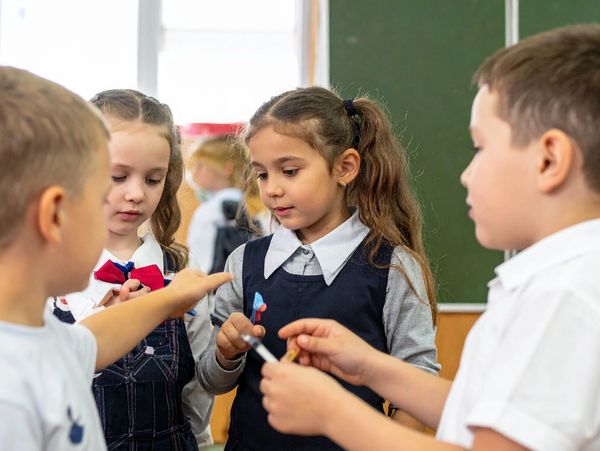 Children in school uniforms sharing and playing with small toys in a classroom.