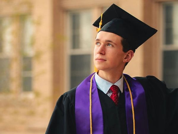 Young man in graduation attire looking upward thoughtfully.
