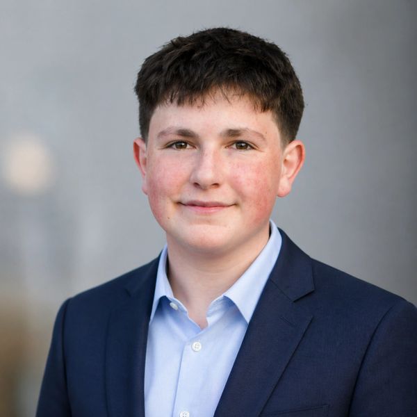 Teenage boy in a blue suit jacket and light blue shirt smiling gently.