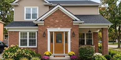 A charming two-story house with brick and beige siding, featuring a double front door and landscaped garden.