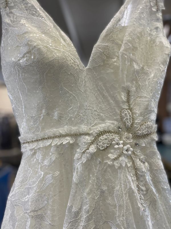 Close-up of a white lace wedding dress with intricate bead and sequin floral embellishments.
