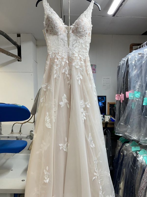 Elegant white wedding dress with floral lace details hanging indoors.