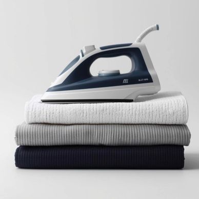 A modern iron resting on neatly folded clothes in white, gray, and navy blue.