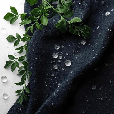 Water droplets on dark fabric with green leaves beside it.