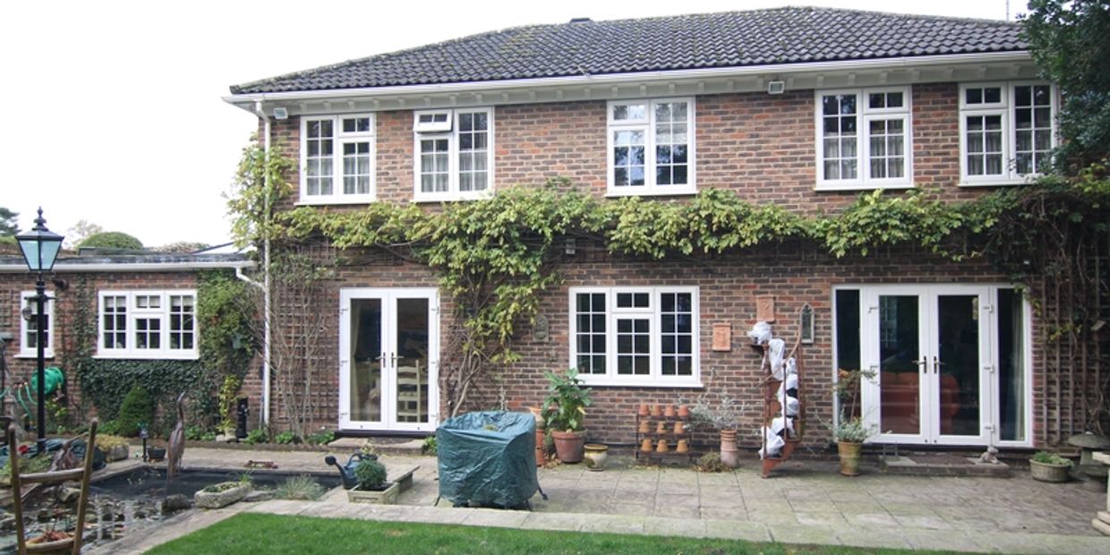 Two-story brick house with patio and garden, featuring white-framed windows and climbing plants.