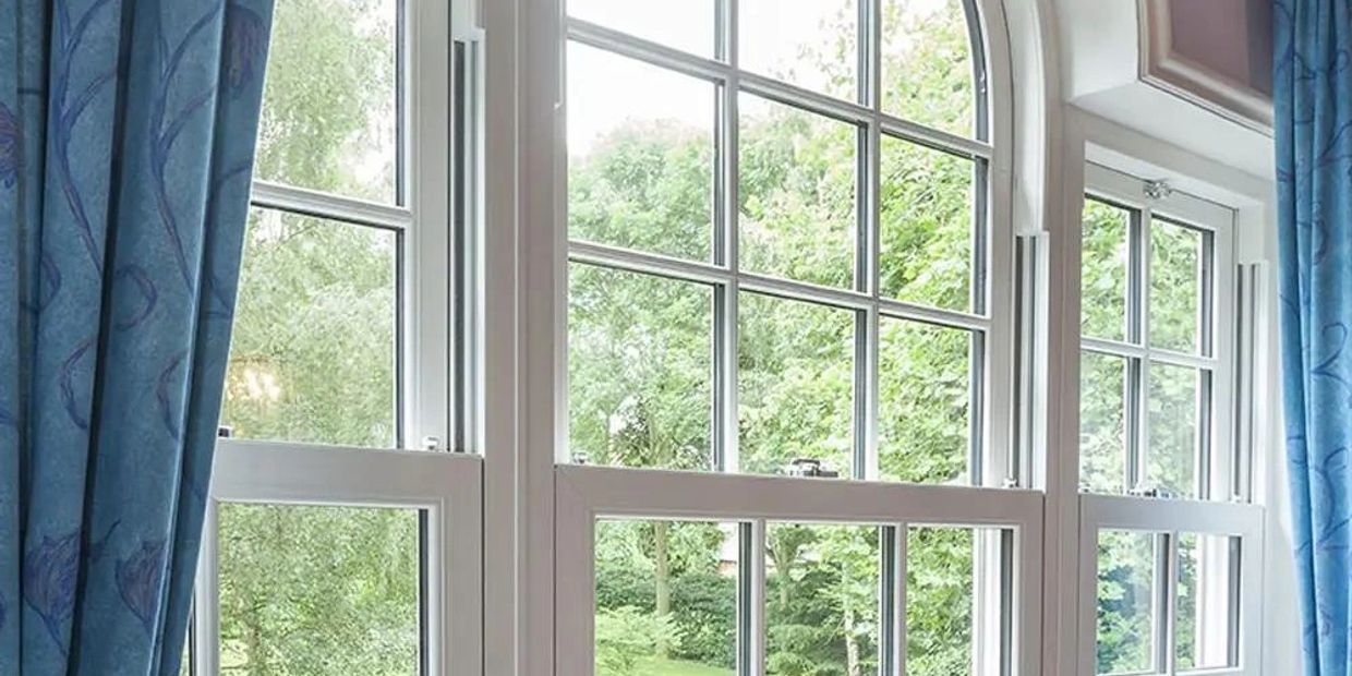 White framed windows with blue curtains overlooking a green garden.