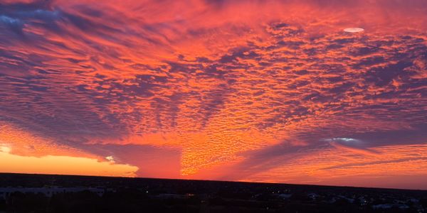 Vibrant orange and purple sunset with textured clouds over a silhouetted landscape.