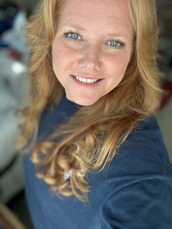 Smiling woman with blue eyes and long blonde hair in a navy blue shirt.