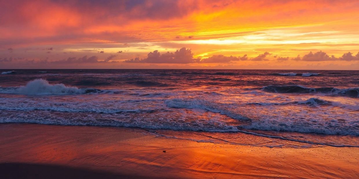 A vibrant sunset over ocean waves and sandy beach.