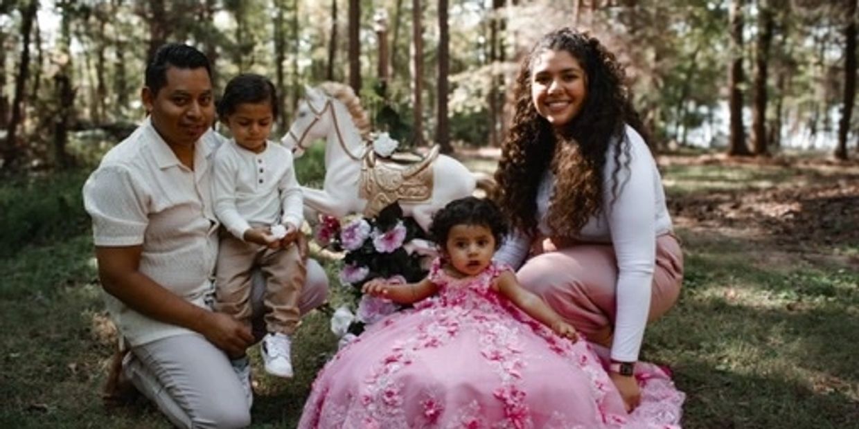 A happy family with two kids poses outdoors beside a decorative rocking horse.