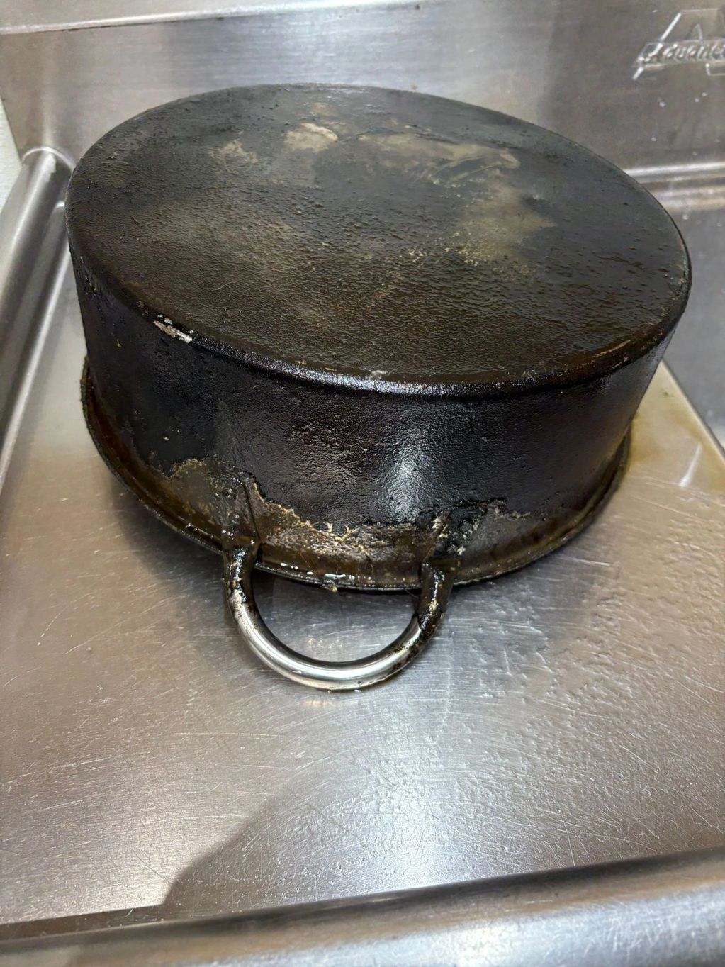 Burnt and heavily stained cooking pot with a metal handle.