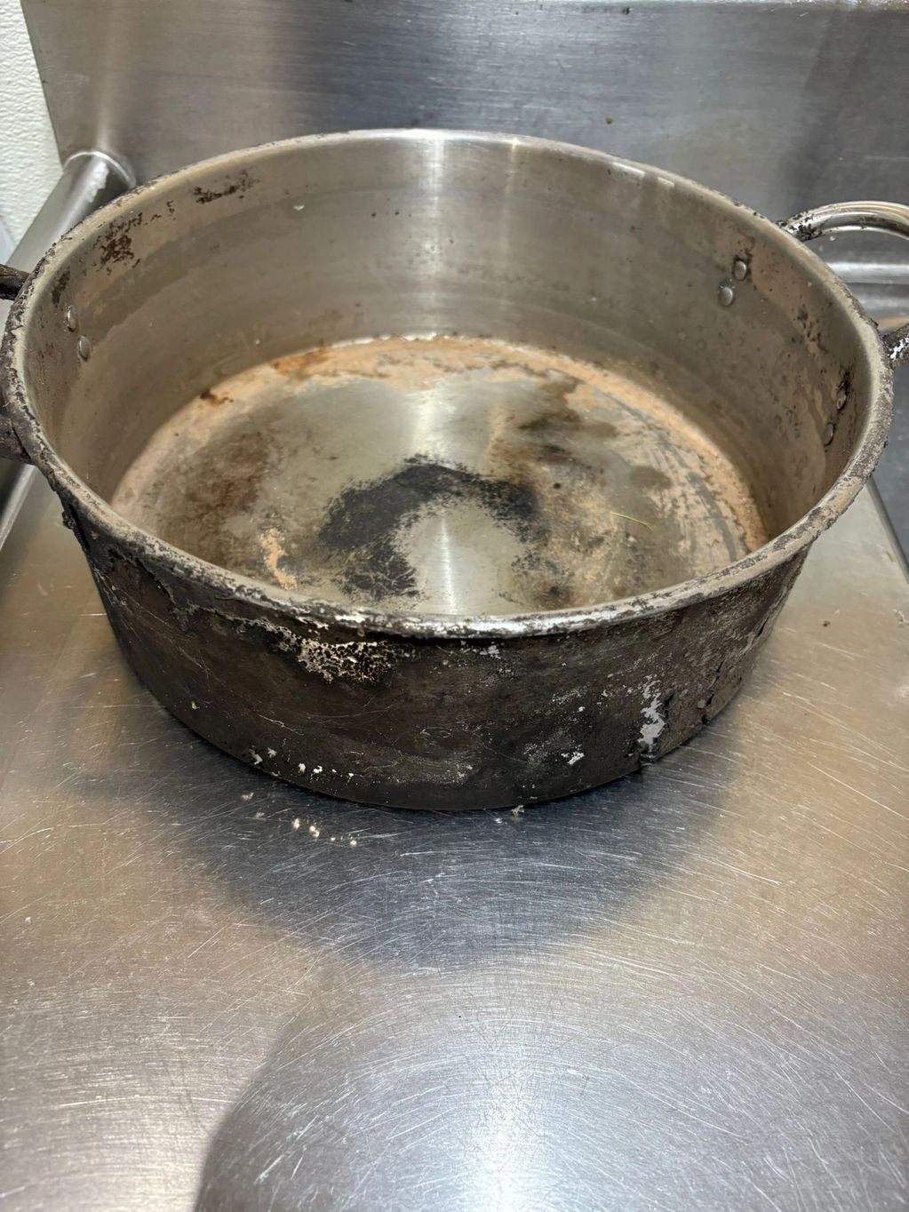 Worn and stained metal cooking pot on a stainless steel surface.