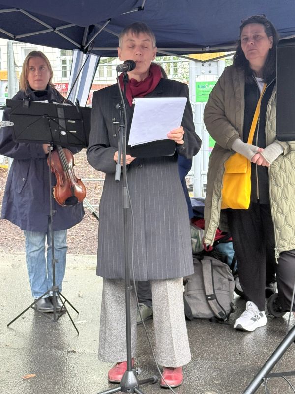 Woman reading from sheet at outdoor event under canopy.