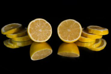 Symmetrical lemon halves and slices on a reflective surface.