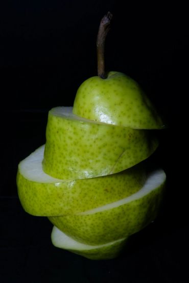 Sliced green pear stacked with a dark background.