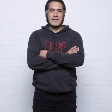 Man standing with arms crossed, wearing a black hoodie.