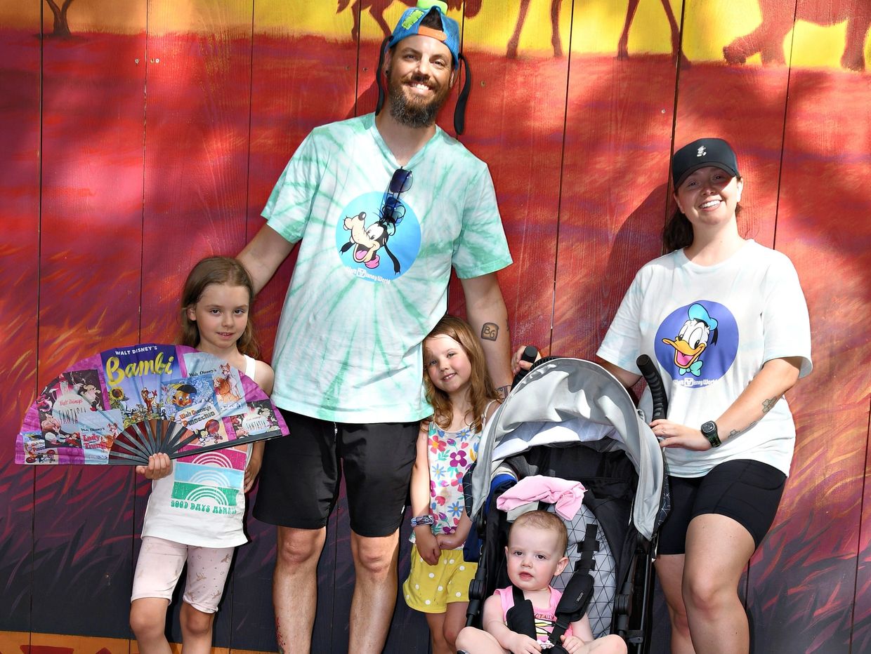 Family of five posing happily in front of a colorful animal mural at a theme park.