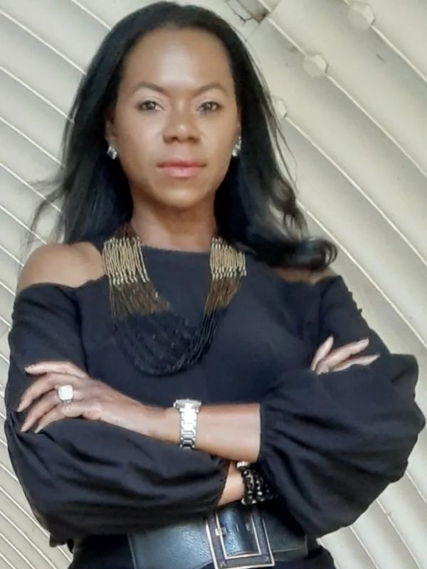 Confident woman in black with arms crossed, wearing statement jewelry.