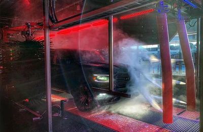Truck going through car wash with red lights shining on truck as it is sprayed with jets of water.