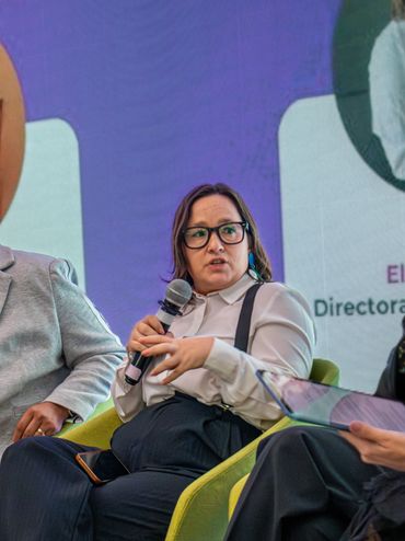 Mujer hablando en panel con micrófono en mano.