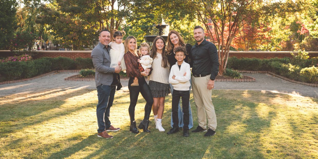 A multi-generational family portrait outdoors on a sunny day.
